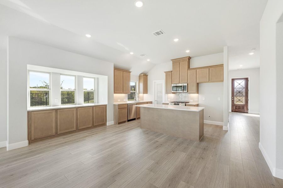 Open kitchen with light wood cabinets, center island, white countertops, and light hardwood floors