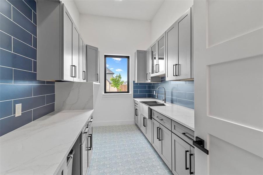 Kitchen with tasteful backsplash, gray cabinets, light stone counters, light tile floors, and sink