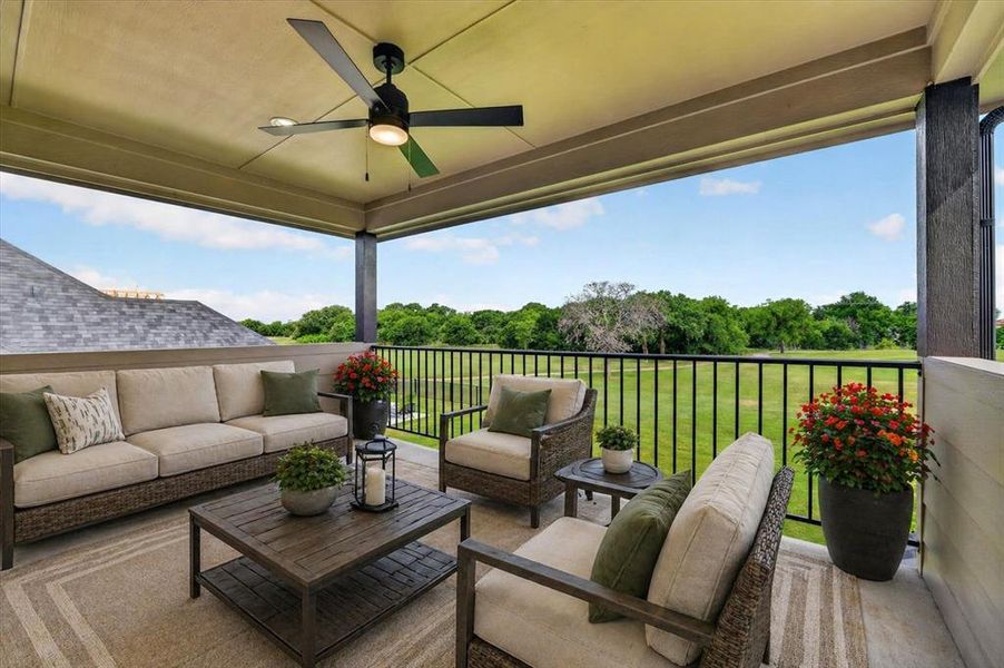 Covered outdoor patio with a ceiling fan, featuring a concrete surface and black metal railings overlooking a green expanse