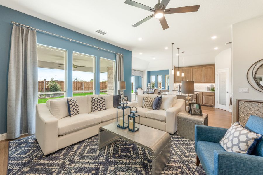 Open-concept living room with blue accent wall, ceiling fan, and cream sofas, open to kitchen with wood cabinets.