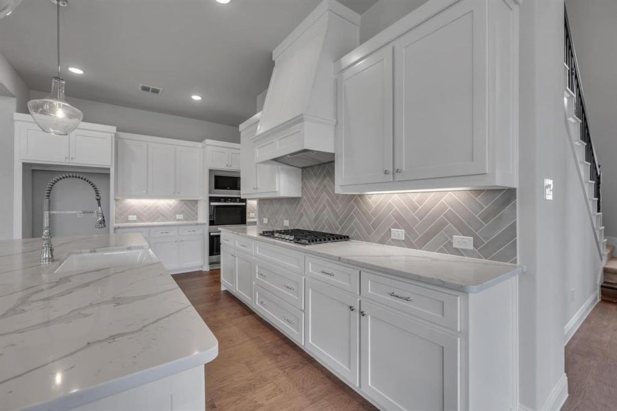 Kitchen featuring sink, decorative light fixtures, wood-type flooring, and white cabinets