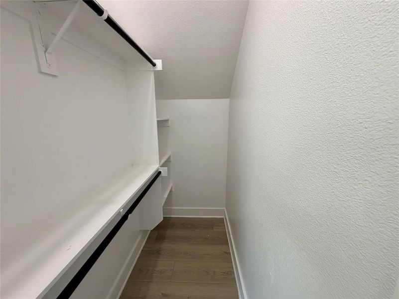 Walk-in closet featuring built-in shelving, two hanging rods, white trim, and wood-finish flooring Walk-in closet featuring built-in shelving, two hanging rods, white trim, and wood-finish flooring