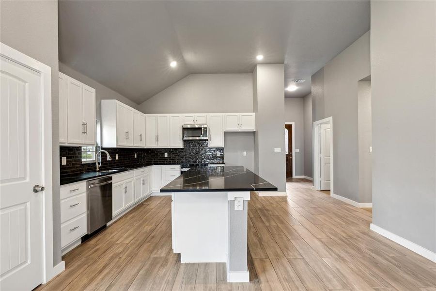 Kitchen with white cabinetry, backsplash, stainless steel appliances, a center island, and light hardwood / wood-style floors