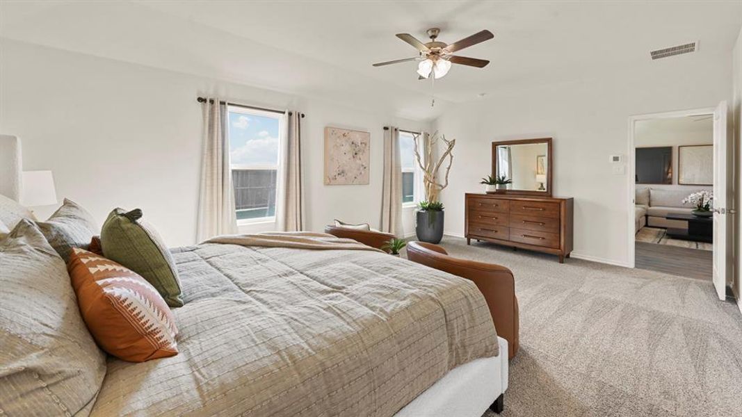 Spacious bedroom featuring light-toned carpet, a ceiling fan, and two windows providing natural light