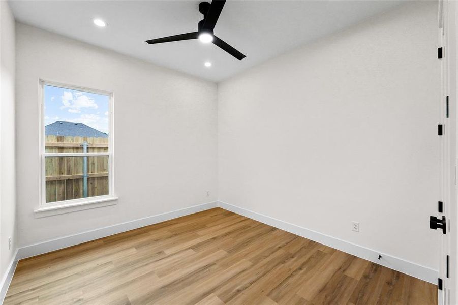 Room featuring neutral wall tones, wood-finish flooring, a white-framed window, and a black ceiling fan with integrated lighting