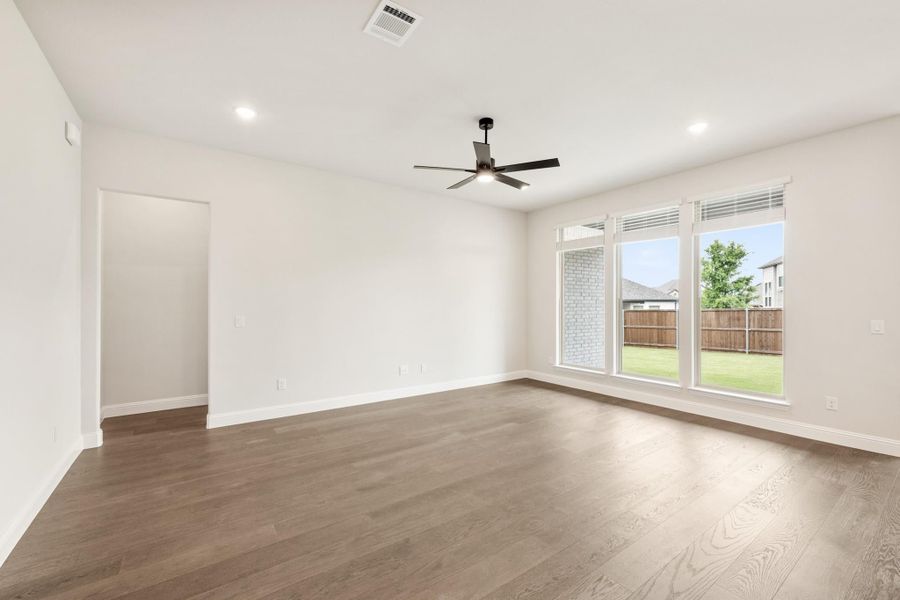 Empty living room with hardwood floors, ceiling fan, and large windows overlooking a backyard Empty living room with hardwood floors, ceiling fan, and large windows overlooking a backyard