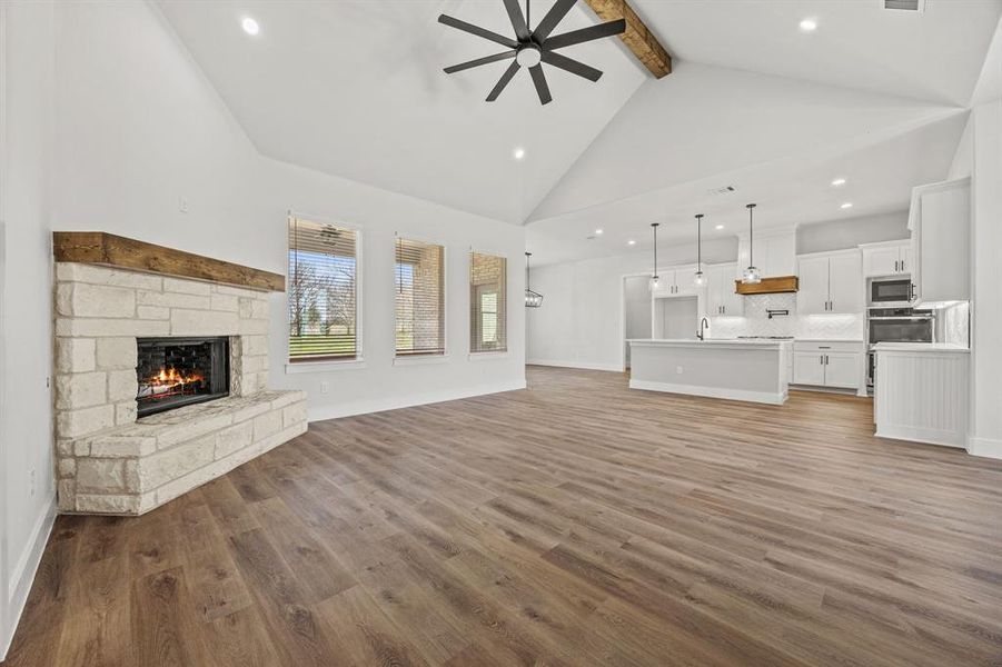 Unfurnished living room with beamed ceiling, a stone fireplace, wood finished floors, a ceiling fan, and high vaulted ceiling Unfurnished living room with beamed ceiling, a stone fireplace, wood finished floors, a ceiling fan, and high vaulted ceiling
