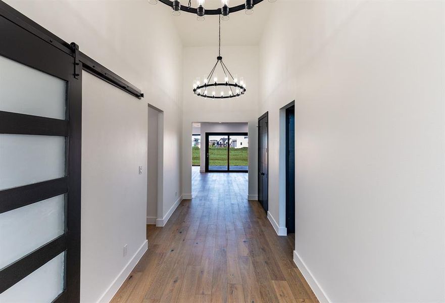 Corridor with white oak flooring, a 12 ft c ustom door, a towering ceiling, and an inviting chandelier