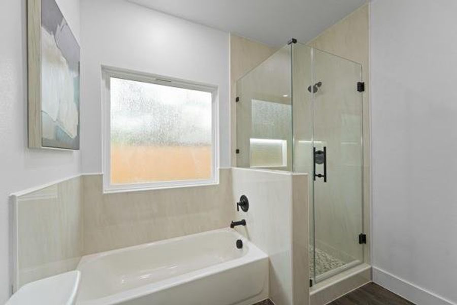 Bathroom featuring a glass-enclosed shower with pebble flooring and a built-in niche, a white soaking tub with matte black fixtures, and a privacy window Bathroom featuring a glass-enclosed shower with pebble flooring and a built-in niche, a white soaking tub with matte black fixtures, and a privacy window