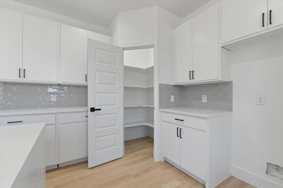 Kitchen featuring backsplash, light countertops, light wood-style flooring, and white cabinetry