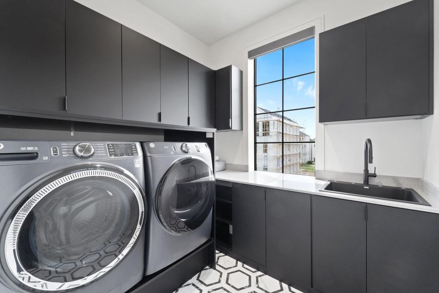 The laundry room features sleek black cabinetry and appliances, complemented by a bright window and stylish geometric tile flooring. A spacious sink and ample counter space enhance both functionality and design. The laundry room features sleek black cabinetry and appliances, complemented by a bright window and stylish geometric tile flooring. A spacious sink and ample counter space enhance both functionality and design.