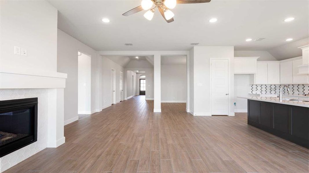 Unfurnished living room with a tiled fireplace, light hardwood / wood-style flooring, sink, lofted ceiling, and ceiling fan