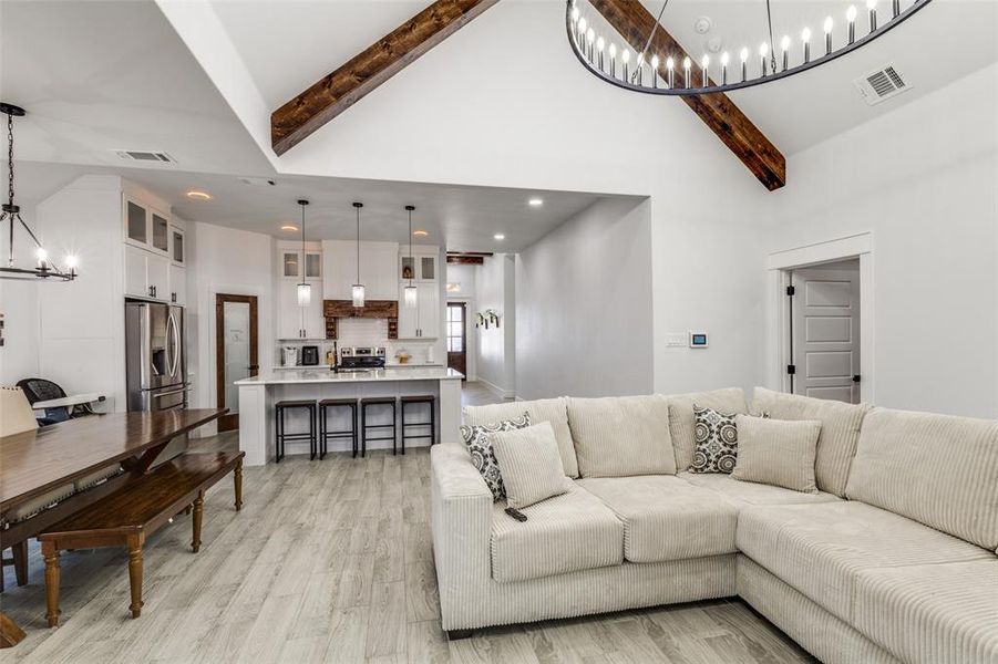 Living room featuring beam ceiling, visible vents, and a notable chandelier