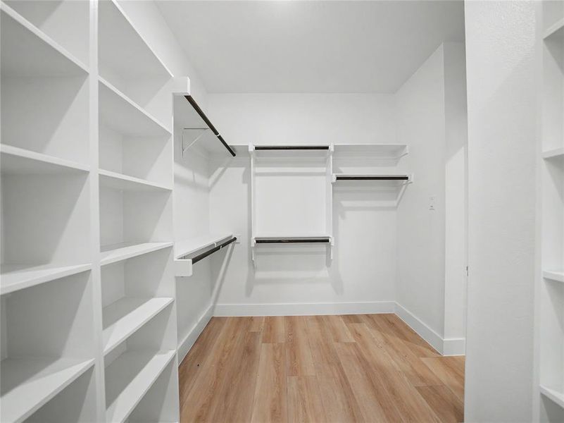 Walk-in closet featuring extensive built-in shelving, multiple hanging rods, crisp white finishes, and wood-finish flooring Walk-in closet featuring extensive built-in shelving, multiple hanging rods, crisp white finishes, and wood-finish flooring