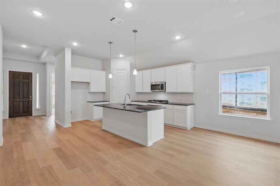 Kitchen featuring a center island with sink, white cabinetry, pendant lighting, stainless steel microwave, and light wood finished floors