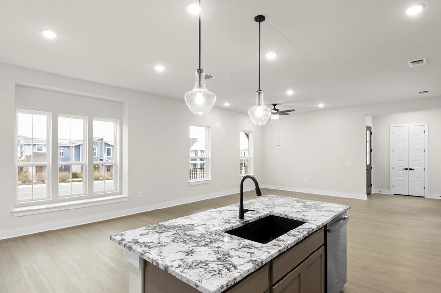 Kitchen featuring recessed lighting, open floor plan, a kitchen island with sink, light stone counters, and hanging light fixtures