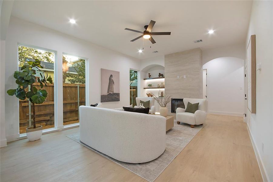 Living area with a tiled fireplace, light wood-style floors, ceiling fan, recessed lighting, and arched walkways