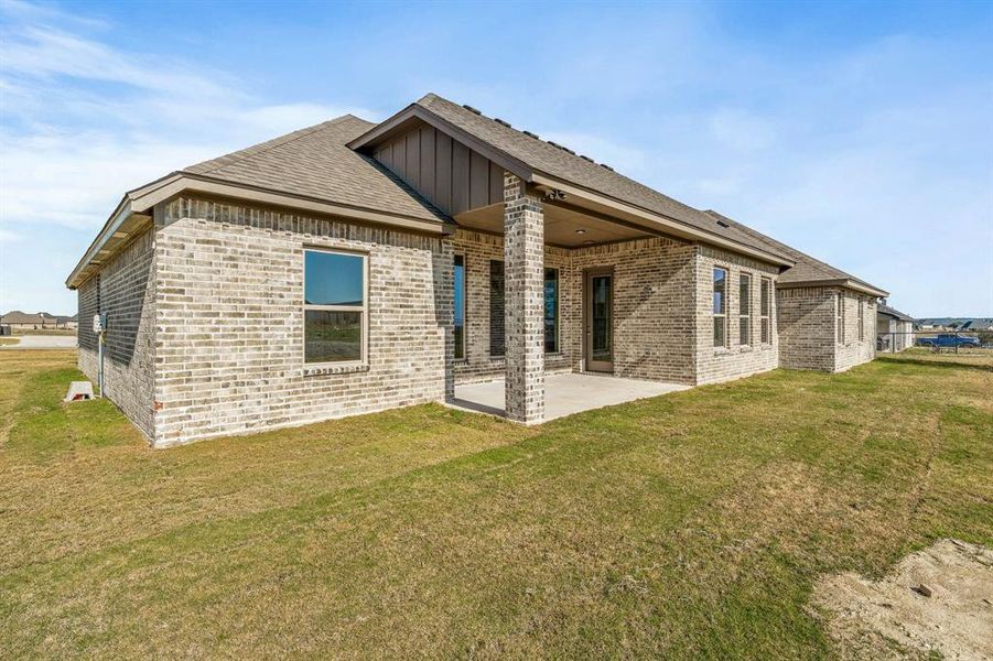 Back of property with a lawn, a patio area, brick siding, board and batten siding, and a shingled roof