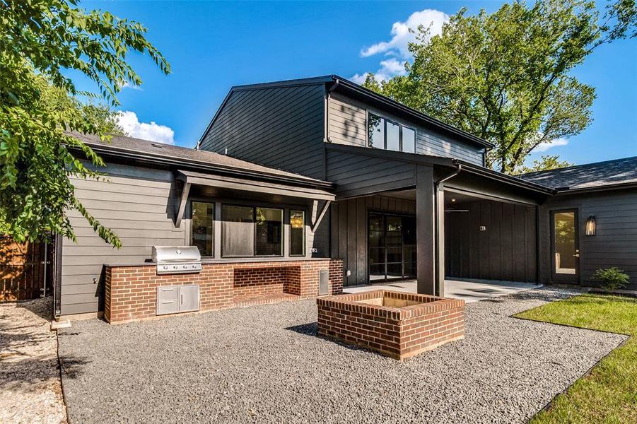 Exterior featuring dark-toned siding, a built-in brick fire pit, a built-in brick grilling station with stainless steel appliances, a covered patio, and large windows Exterior featuring dark-toned siding, a built-in brick fire pit, a built-in brick grilling station with stainless steel appliances, a covered patio, and large windows