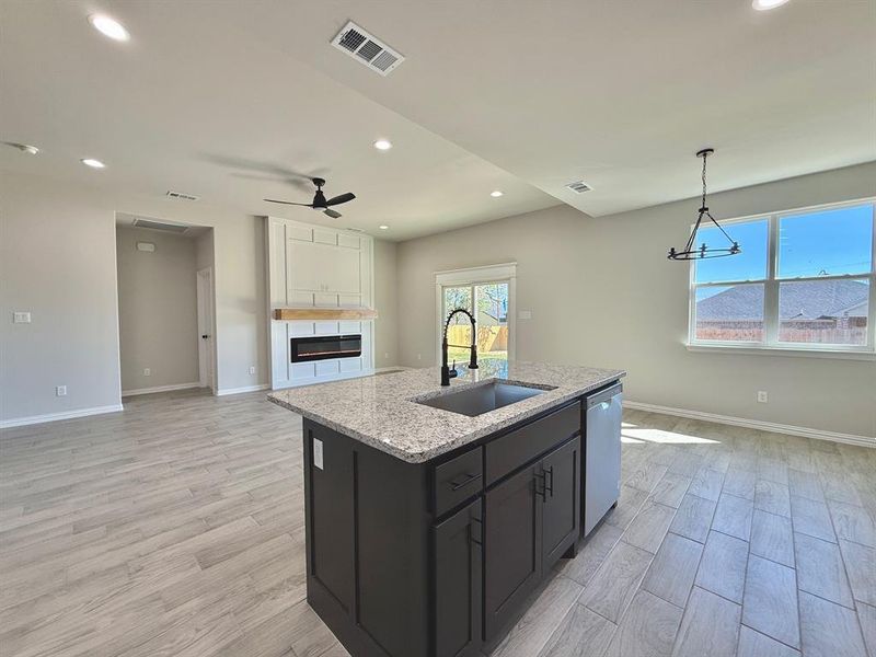 Kitchen featuring light hardwood / wood-style floors, sink, an island with sink, stainless steel dishwasher, and light stone countertops