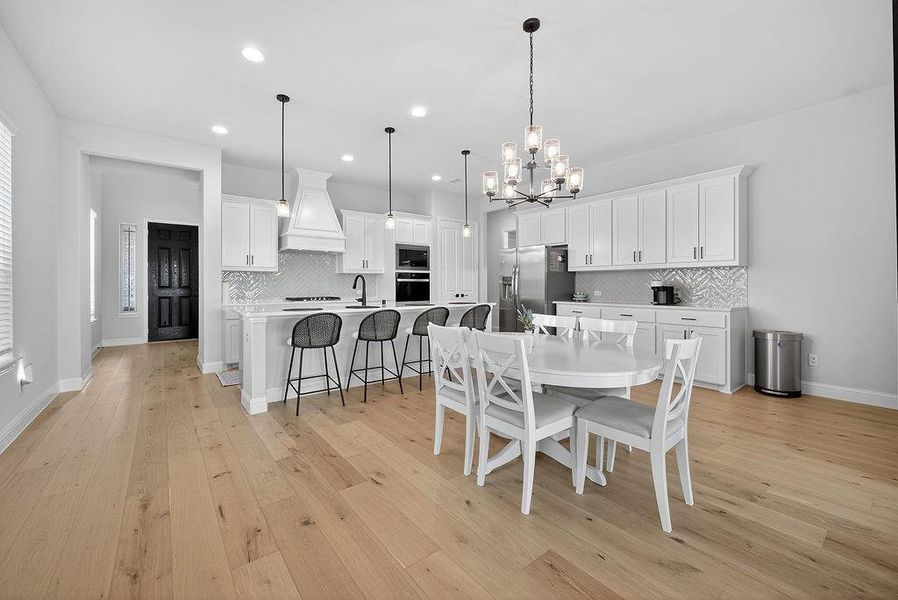 Open-concept kitchen and dining area featuring light wood-finish flooring, white cabinetry, and a textured tile backsplash