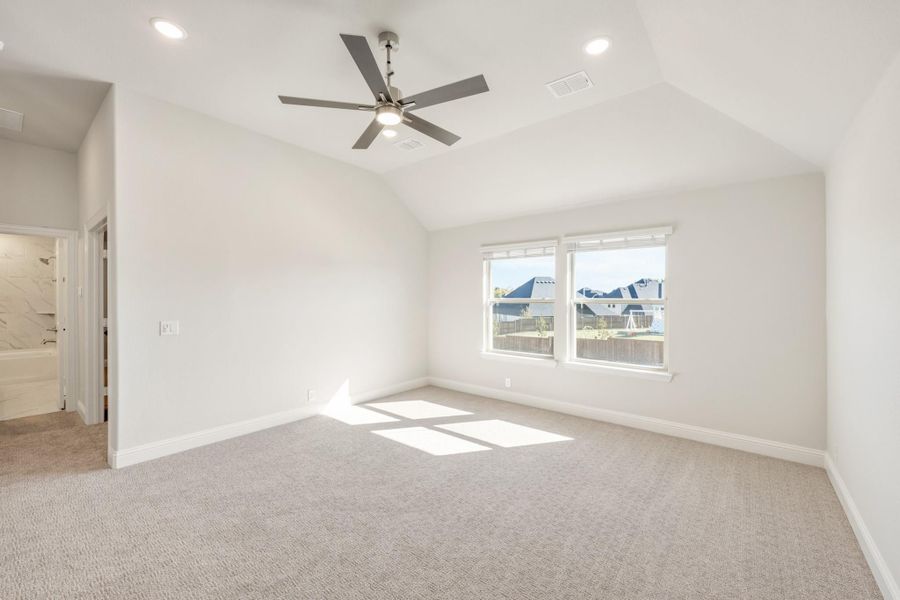 Empty bedroom with vaulted ceiling, ceiling fan, carpet flooring, and ensuite bathroom doorway Empty bedroom with vaulted ceiling, ceiling fan, carpet flooring, and ensuite bathroom doorway