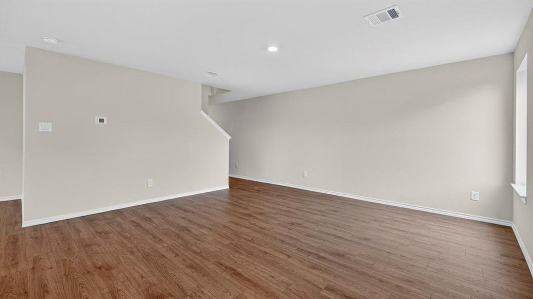 Spacious room featuring wood-finish flooring, light-toned walls, recessed lighting, and a white trim baseboard