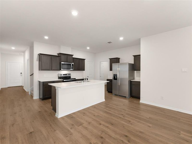 Kitchen with dark brown cabinetry, appliances with stainless steel finishes, a kitchen island with sink, and light wood-type flooring