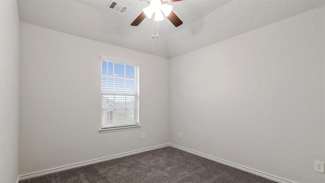 Empty room featuring dark colored carpet, a ceiling fan, and vaulted ceiling