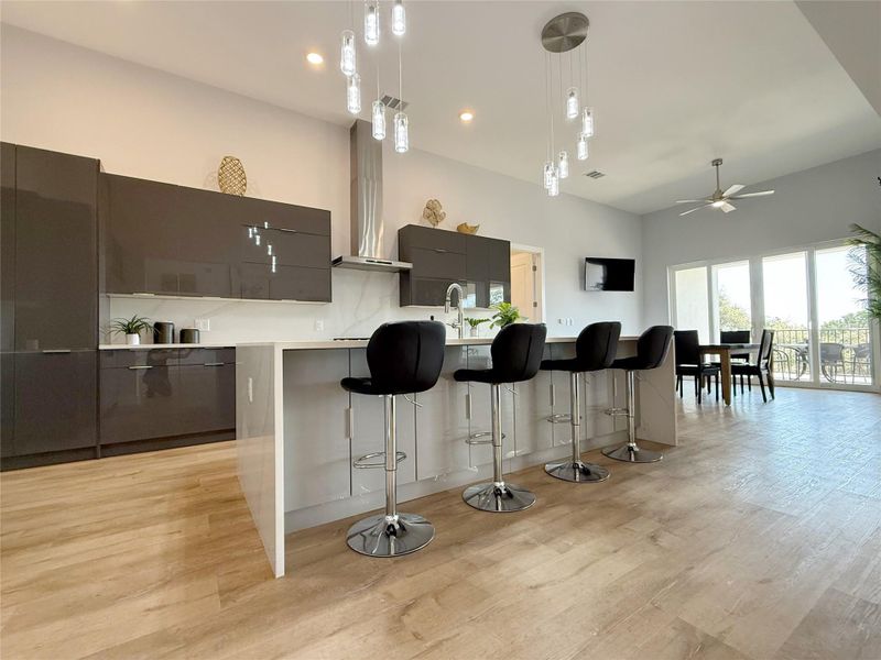 Kitchen featuring modern cabinets, hanging light fixtures, a kitchen bar, wall chimney range hood, and a large island with sink