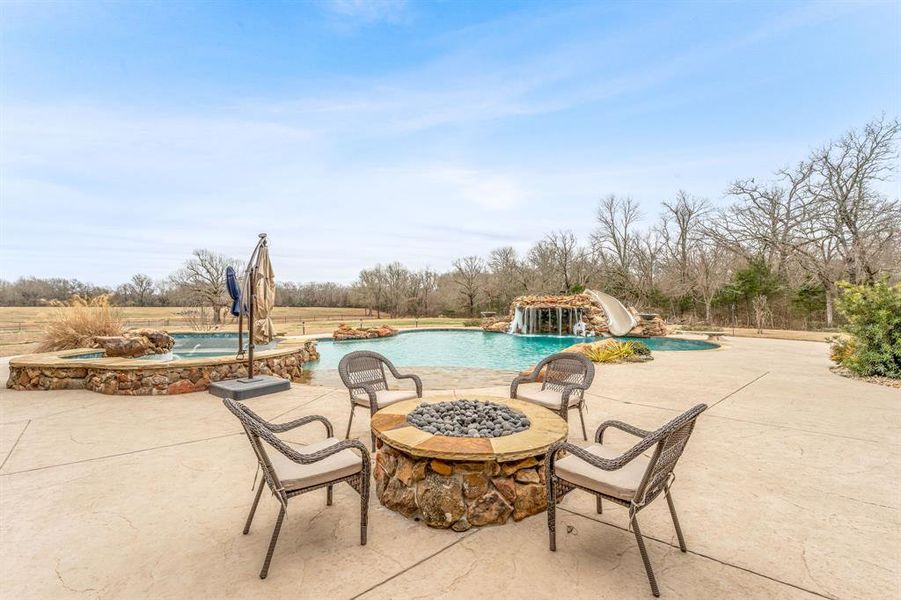 View of patio featuring a fire pit, an outdoor pool, and an in-ground hot tub
