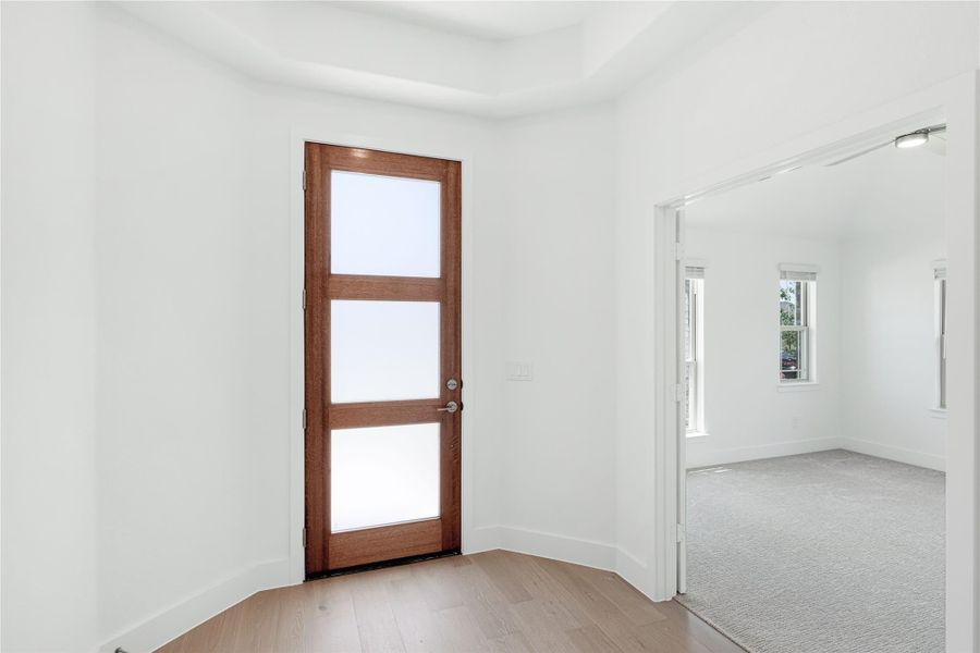 Bright room with wood and frosted glass panel door, hardwood floors, and open doorway to carpeted bedroom