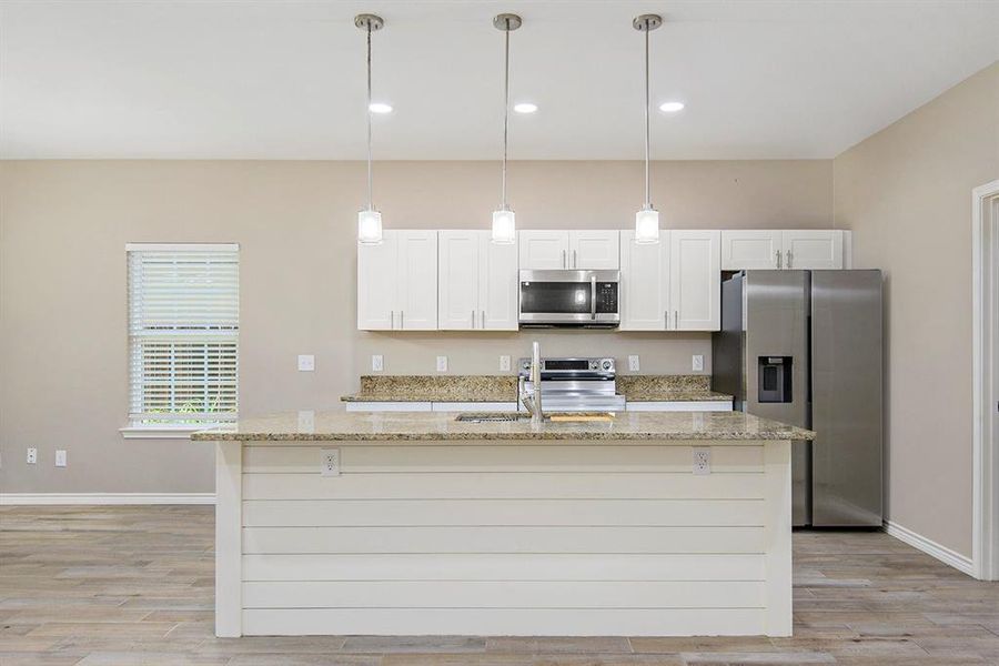 Kitchen with stainless steel appliances, a kitchen island with sink, light wood-style flooring, light stone counters, and recessed lighting