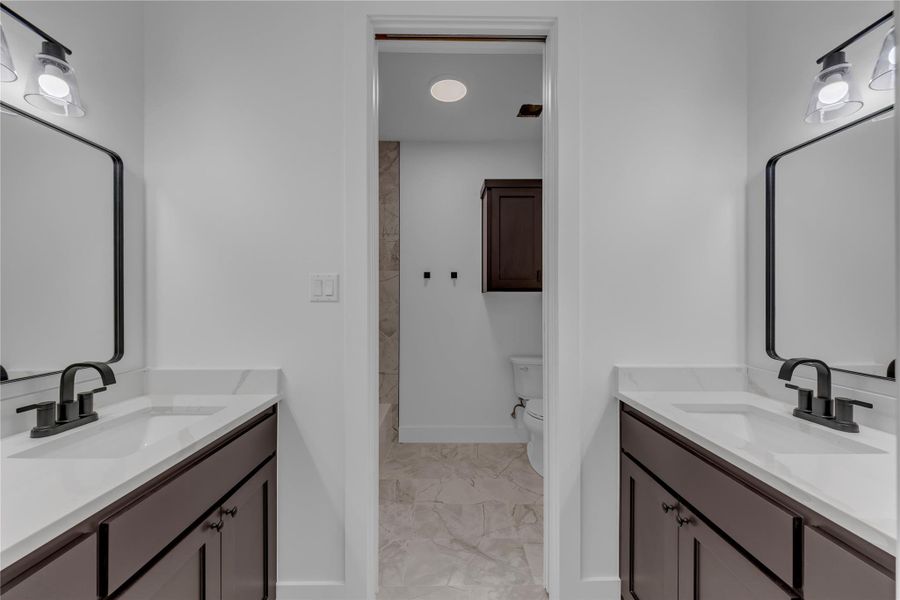 Guest Bath; Dual vanities with modern dark hardware flank the entrance to a tiled private bathroom.