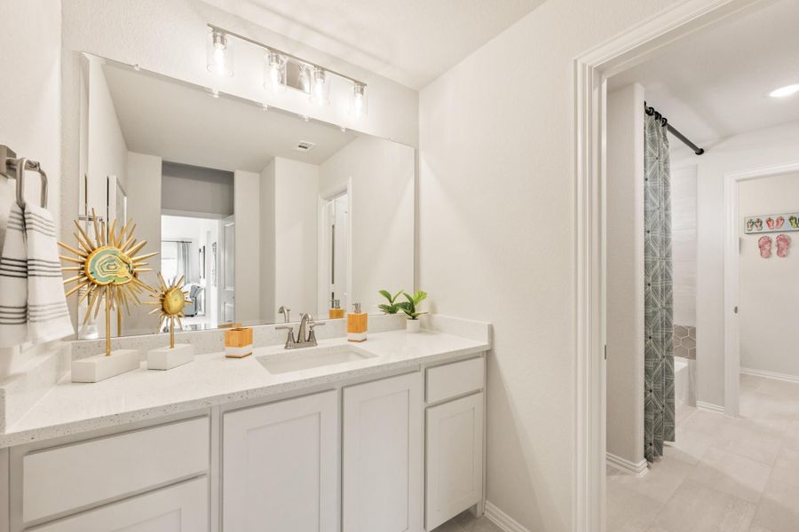 Bathroom with white vanity, quartz countertop, large mirror, and separate shower area with curtain visible through doorway. Bathroom with white vanity, quartz countertop, large mirror, and separate shower area with curtain visible through doorway.