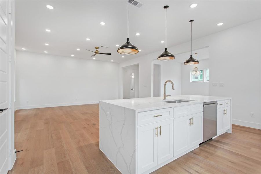 Kitchen featuring white cabinets, dishwasher, a kitchen island with sink, light hardwood / wood-style floors, and decorative light fixtures