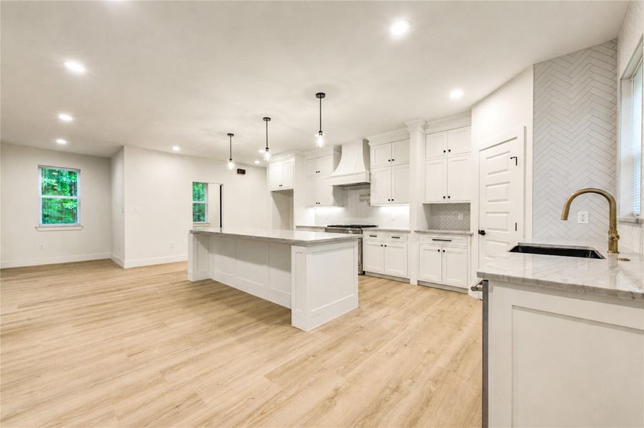 Spacious and elegant kitchen featuring a large island with pendant lighting, sleek white cabinetry, and a six burner gas Forno range.