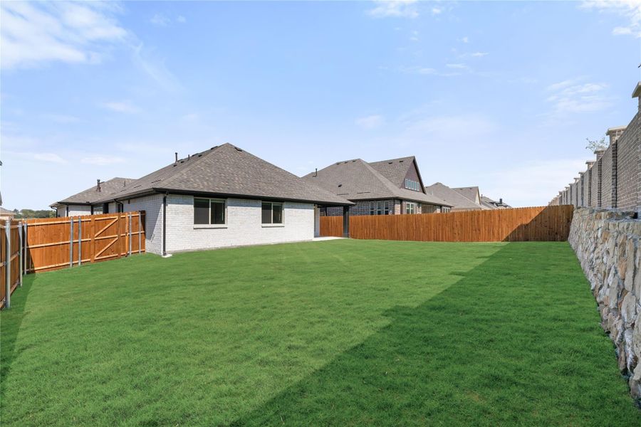 Backyard with large green lawn, wood privacy fence, and brick home exterior Backyard with large green lawn, wood privacy fence, and brick home exterior