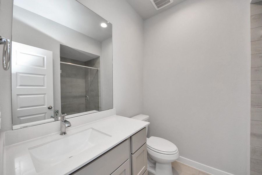 Secondary bath features tile flooring, walk-in shower with tile surround, light stained wood cabinets, beautiful light countertop. Sample photo of completed home with similar floor plan. Actual colors and selections may vary.