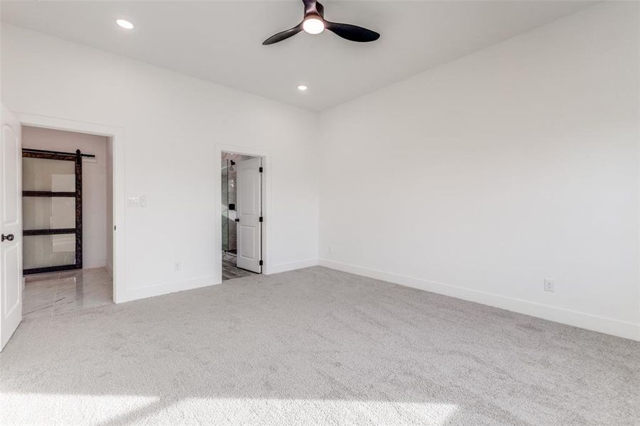 Spare room featuring a barn door, light carpet, and ceiling fan