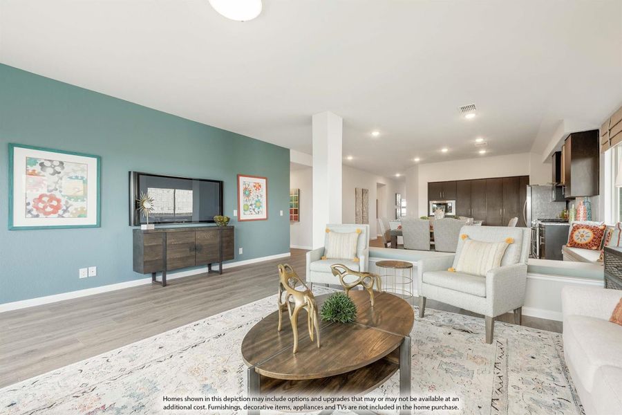 Open-concept living room with teal accent wall, wall-mounted TV, and view into kitchen with dark cabinets Open-concept living room with teal accent wall, wall-mounted TV, and view into kitchen with dark cabinets