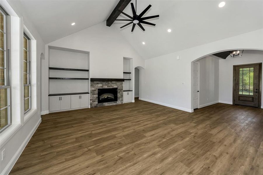 Unfurnished living room featuring beamed ceiling, arched walkways, wood finished floors, a ceiling fan, and a fireplace