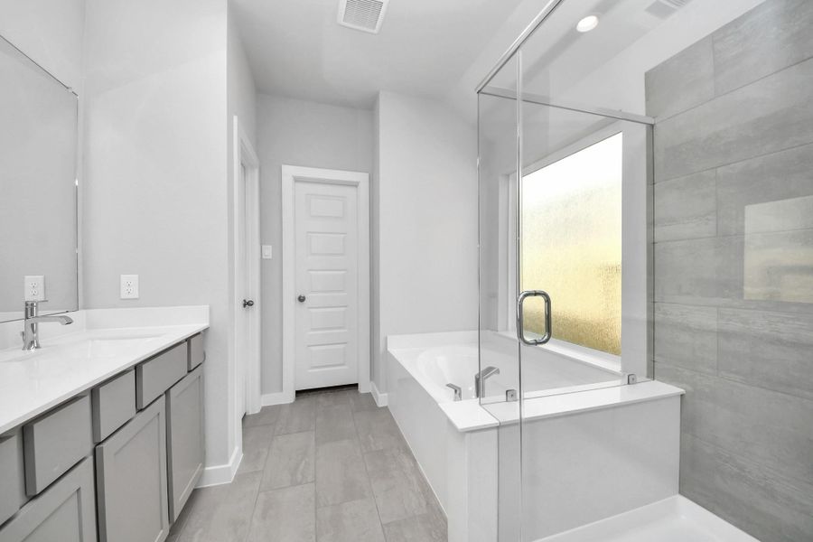 Escape to a spa-like oasis in this primary bathroom. Enjoy a walk-in shower with tile surround, a separate garden tub with custom detailing, and an elegant vanity featuring light countertops, modern hardware, and beautiful vanity lights. Experience luxury and relaxation in every detail. Sample photo of completed home with similar floor plan. Actual colors and selections may vary. Escape to a spa-like oasis in this primary bathroom. Enjoy a walk-in shower with tile surround, a separate garden tub with custom detailing, and an elegant vanity featuring light countertops, modern hardware, and beautiful vanity lights. Experience luxury and relaxation in every detail. Sample photo of completed home with similar floor plan. Actual colors and selections may vary.