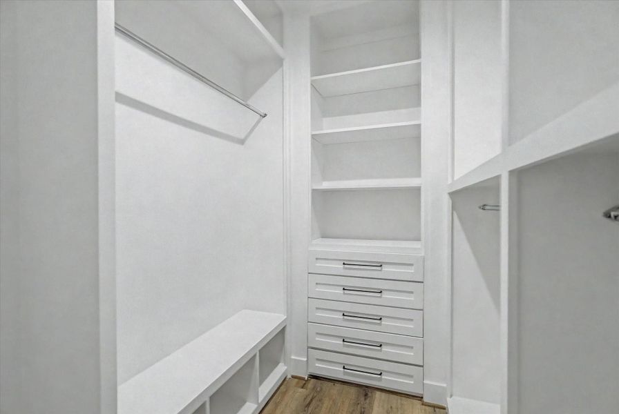Custom primary closet featuring built-in drawers and ample hanging space.