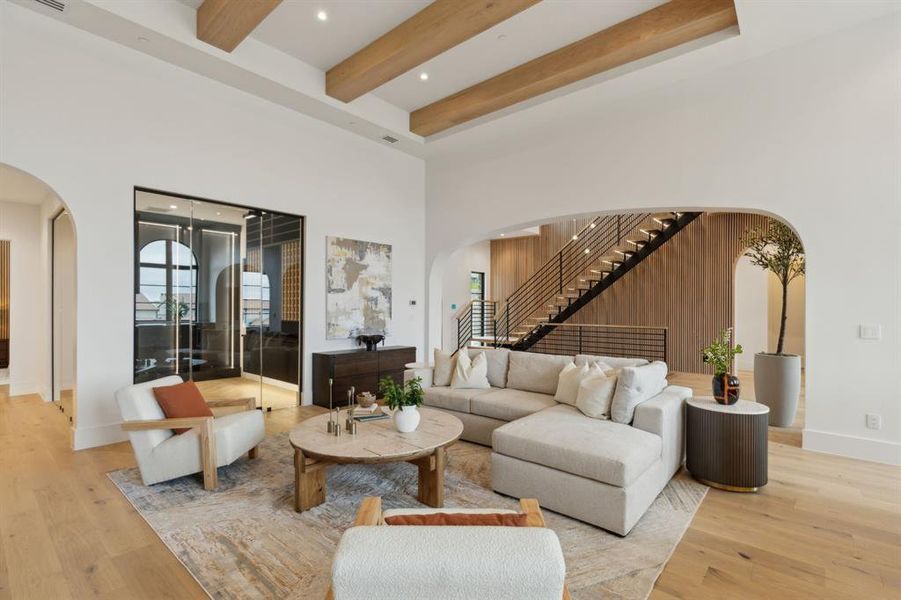 Living room featuring arched walkways, stairway, beamed ceiling, white oak wood flooring, a wine cellar, wood accents on wall, Floating staircase, iron hand rail , and a high ceiling Living room featuring arched walkways, stairway, beamed ceiling, white oak wood flooring, a wine cellar, wood accents on wall, Floating staircase, iron hand rail , and a high ceiling
