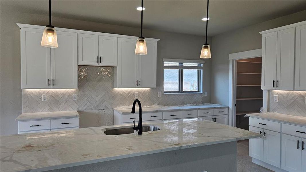 Kitchen featuring decorative backsplash, light stone countertops, and decorative light fixtures