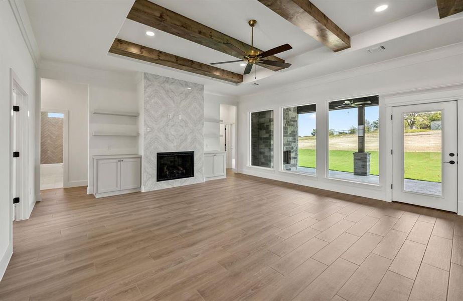 Unfurnished living room with a ceiling fan, light wood-style floors, a premium fireplace, beam ceiling, and recessed lighting Unfurnished living room with a ceiling fan, light wood-style floors, a premium fireplace, beam ceiling, and recessed lighting