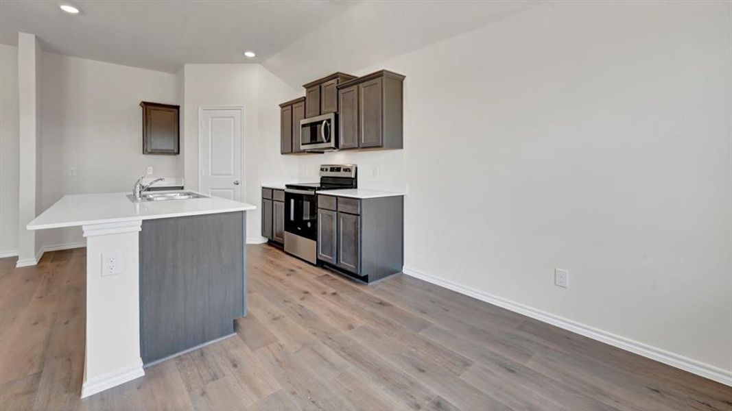 Kitchen featuring a central island with an undermount sink, white countertops, dark gray cabinetry, stainless steel appliances, and wood-finish flooring