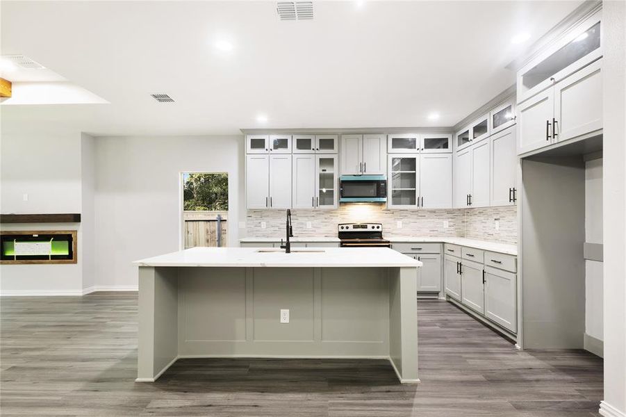 Kitchen featuring tasteful backsplash, appliances with stainless steel finishes, dark wood-type flooring, a center island with sink, and recessed lighting