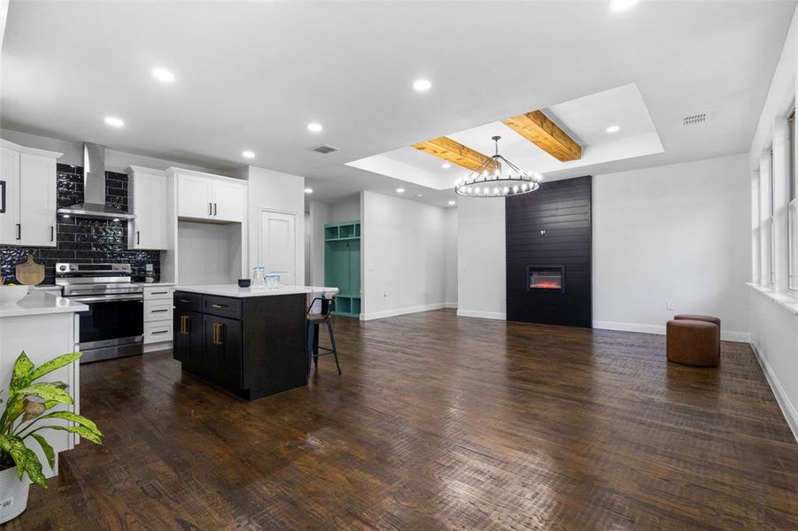 Kitchen featuring electric stove, wall chimney exhaust hood, a tray ceiling, open floor plan, and light countertops Kitchen featuring electric stove, wall chimney exhaust hood, a tray ceiling, open floor plan, and light countertops